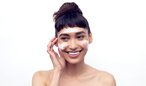 Model with hair in bun, smiling as she applies product to face