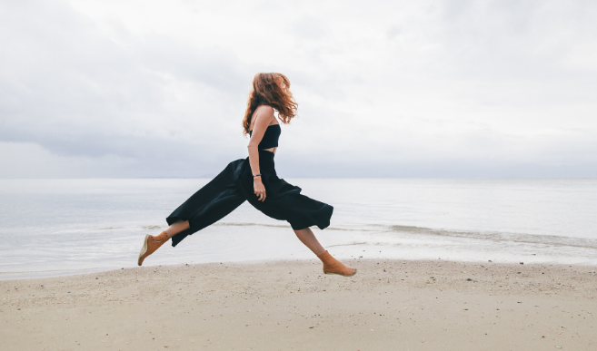 Women caught in midair jump across sandy beach